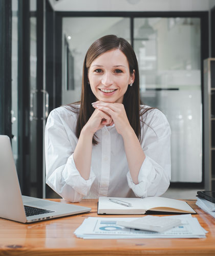 Mujer sonriente sentada a una mesa con un portátil y documentos con gráficos